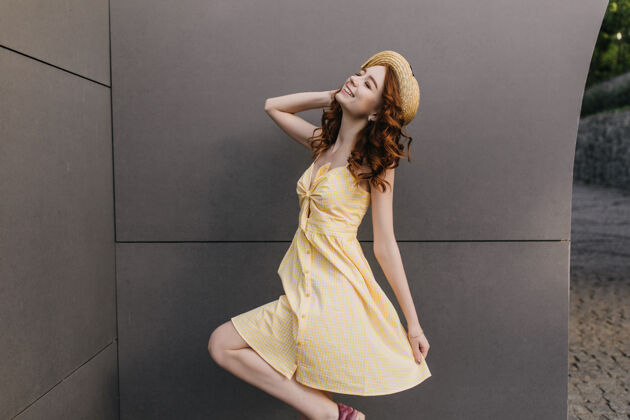 肖像热情的红发女孩戴着复古草帽在灰色的墙上跳舞身着黄色服装的快乐卷发女士的室内照片时尚欢快优雅