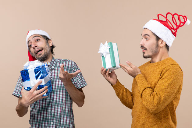 伙计们正面图两个不满意的家伙拿着圣诞礼物米色孤立的背景两个男人圣诞节