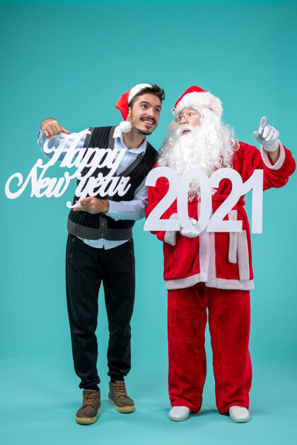 举行圣诞老人的正面图 蓝色墙上的男性手持新年快乐和2021横幅圣诞庆祝快乐