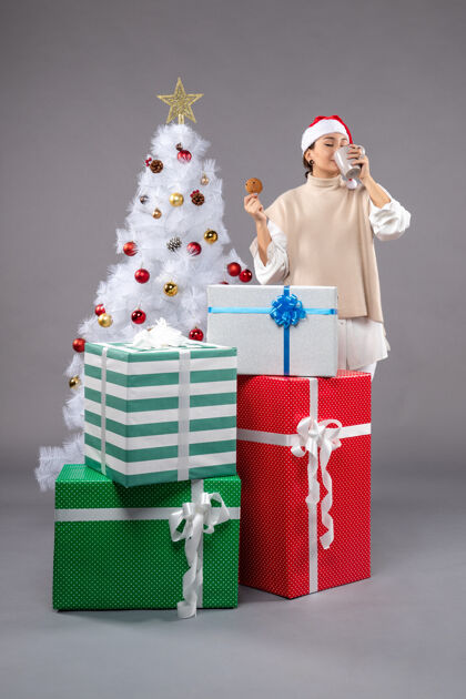 圣诞帽年轻的女人喝着茶 灰色的饼干包包圣诞树