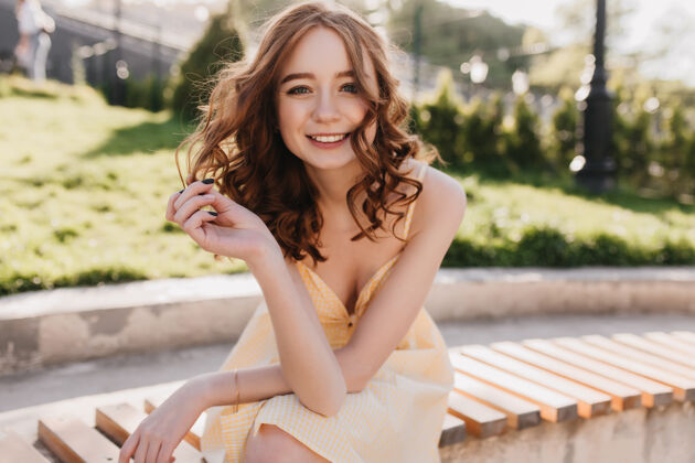 阳光优雅的姜黄色连衣裙女孩坐在公园里可爱的红发卷发女子摆出充满灵感的微笑对大自然肖像人大笑