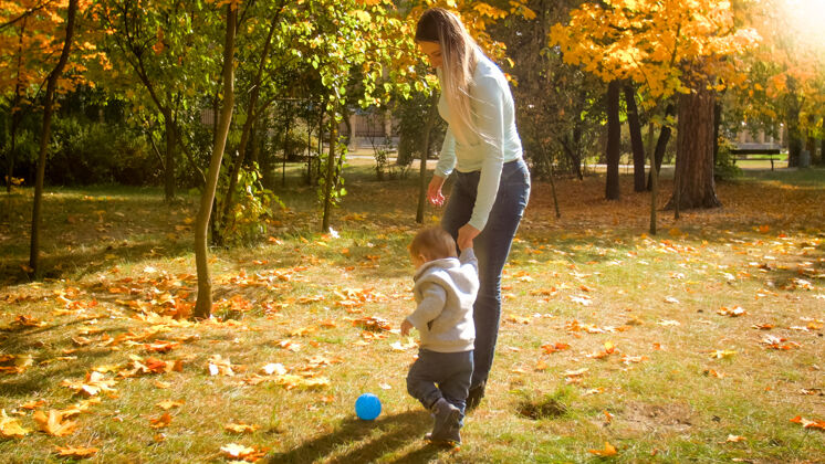 笑可爱的小男孩牵着妈妈的手在秋天公园踢足球人父母一起