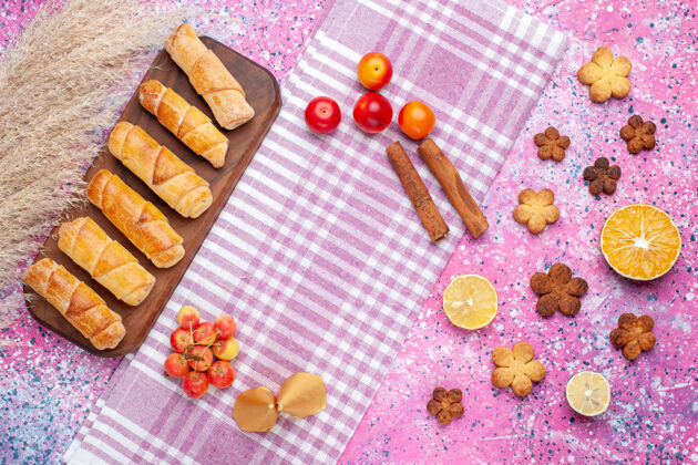 水果在浅粉色的桌子上俯瞰美味的小面包圈和饼干黄色食物糖果