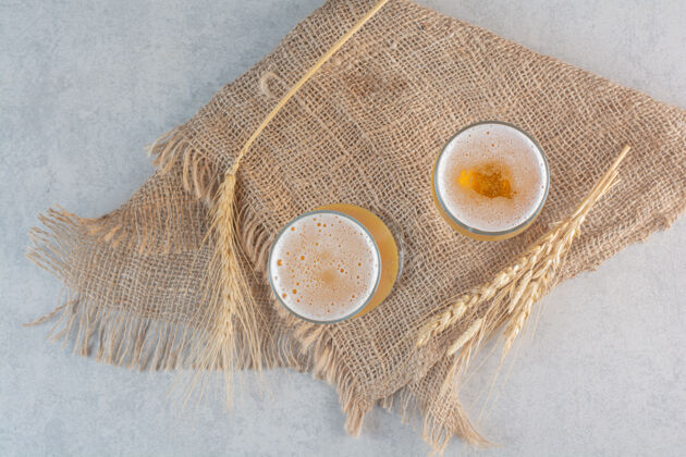 顶视图两杯啤酒和麻布上的小麦罐装啤酒马克杯麦芽酒