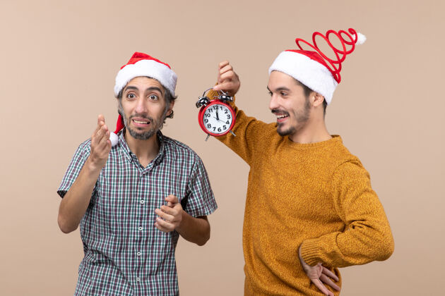 闹钟前视图两个圣诞节男子拿着一个闹钟在米色孤立的背景男人脸帽子