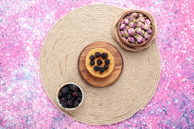 新鲜顶视图新鲜的黑莓放在白色的小罐子里 粉红色的桌子上放着小蛋糕水果浆果粉色