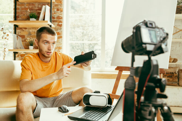 大众年轻的白人男性博主 带着专业设备 在家里录制虚拟现实眼镜的视频评论博客 视频博客 视频博客男人在流媒体直播时评估虚拟现实耳机视频博客广播员媒体