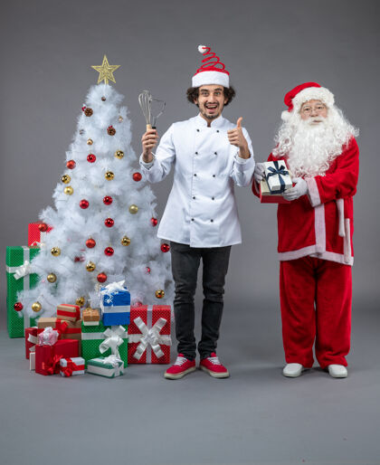庆祝圣诞老人和男厨师在灰色墙上围着圣诞礼物的正视图礼物快乐圣诞快乐