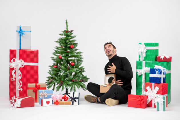 圣诞年轻人坐在白色墙上的节日礼物周围的正面视图装饰模型坐
