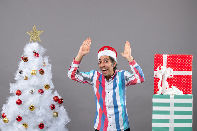 灰色前视图快乐的人把手举到白色圣诞树旁男性树礼物