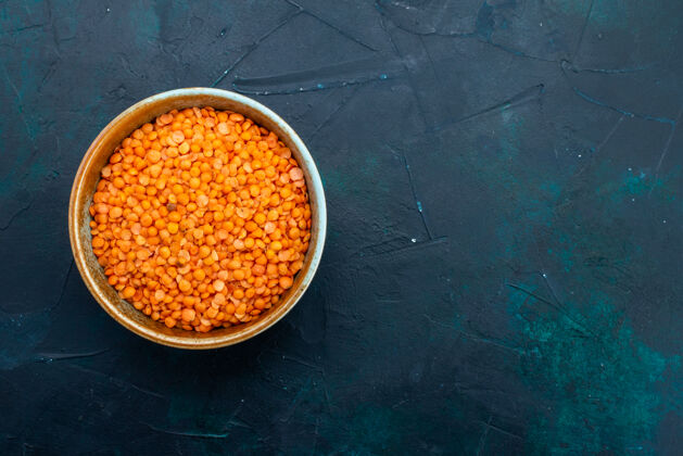 健康深蓝色表面上圆形锅内的生橙色小扁豆俯视图内部烹饪可食用水果