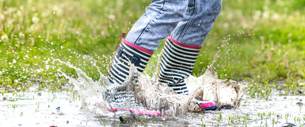 橡胶胶靴在水坑里跳跃的过程中伴随着水花飞溅雨散步雨