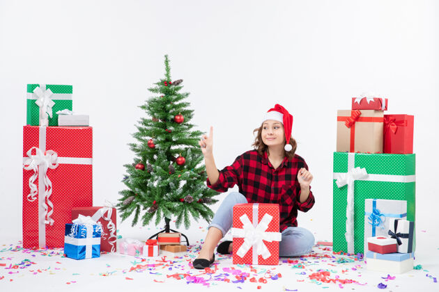 女人年轻女子围坐在礼物和白色墙上的小圣诞树前的视图快乐圣诞快乐人
