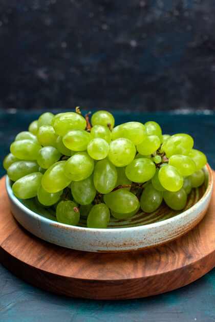 正面在深蓝色桌子上的盘子里 可以看到新鲜的绿色葡萄 醇厚多汁的水果醋栗绿色水果