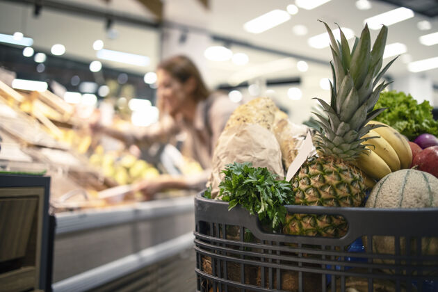 模型特写的购物车在超市里的食品 水果和蔬菜 而在后台妇女采取的产品下架人超市购物车