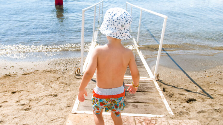 海岸戴著帽子的小男孩在沙灘上的海水里散步腳趾海洋水