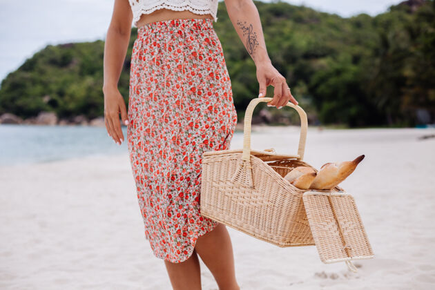 海边沙滩上的浪漫女人穿着裙子 针织上衣 戴着草帽 抱着面包篮子 生态生活面包女人海滩