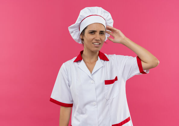 放困惑的年轻女厨师穿着厨师制服把手放在头上孤立的粉红色墙壁与复制空间头年轻厨师