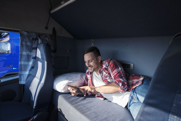 挥手卡车司机躺在床上 通过平板电脑与家人交流卡车卡车司机职业