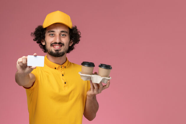 名片正面图：身穿黄色制服和披风的男性信使手持棕色咖啡杯和粉色墙上的卡片手持商务名片