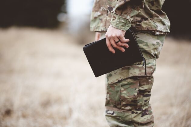战士一个年轻士兵拿着一本圣经在田野里的浅焦镜头军队职业辩护者