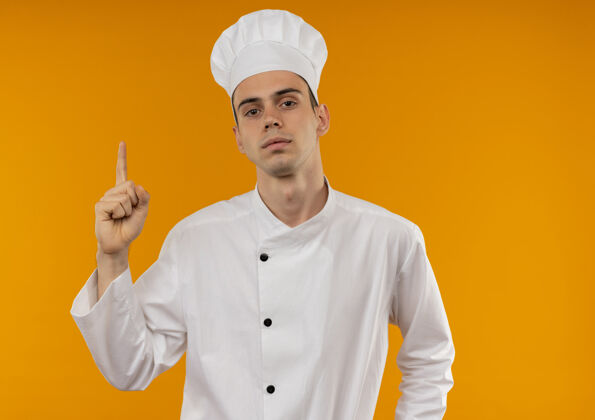手指年轻男酷穿厨师制服点手指向上在隔离的黄色墙壁与复制空间穿看点