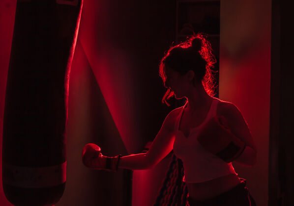 运动轮廓女拳击手拳击手套打拳在黑暗的背景下红色霓虹灯打拳袋模特拳击健身