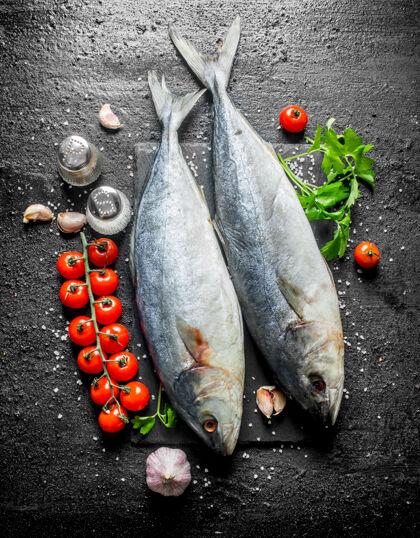 顶视图生鱼放在石头板上 西红柿 欧芹和香料放在黑色的乡村餐桌上生的大蒜海洋