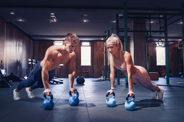 健身这对年轻夫妇正在健身房锻炼漂亮的女人和英俊的肌肉男在现代体育馆里训练在壶铃上做木板举重俯卧撑健身房运动员女孩