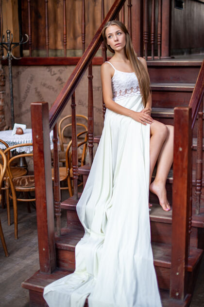 女人年轻体贴的女孩穿着白色长裙坐在楼梯上自然模型长