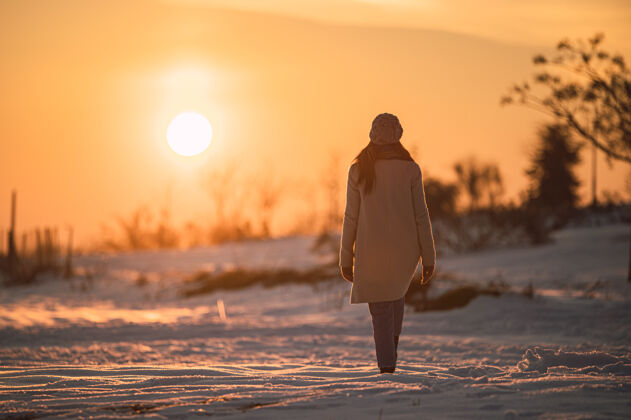 孤独一个穿着暖和衣服的女人独自站在雪白的草地上 欣赏冬日乡间如画的日落时尚全身日落