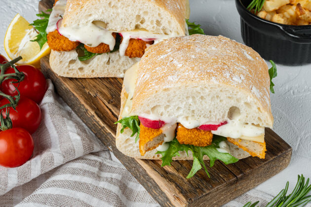 面包汉堡配鱼指新鲜生菜西红柿和鞑靼酱放在木制砧板上奶酪三明治自制