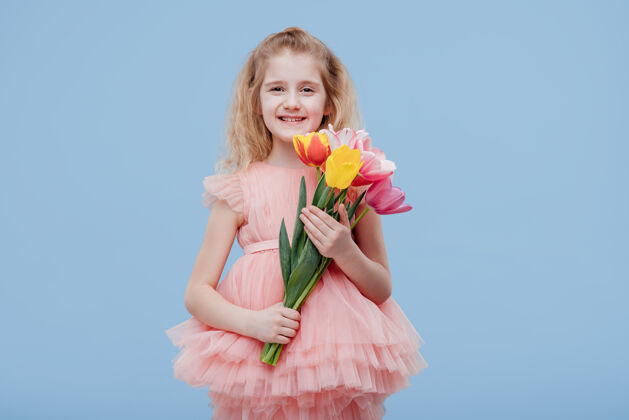 花微笑的小女孩手里拿着春天的郁金香 穿着粉红色的裙子 孤零零地站在蓝色的墙上裙子微笑衣服