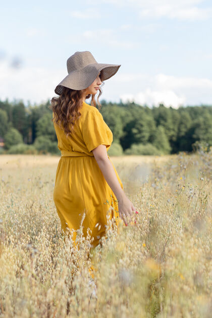 母亲在一个阳光明媚的夏日 一位年轻漂亮的孕妇穿着黄色的裙子 戴着黄色的帽子 走过一片麦田欢呼人收获