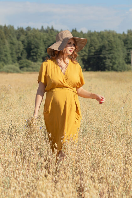 肚子在一个阳光明媚的夏日 一位年轻漂亮的孕妇穿着黄色的裙子 戴着黄色的帽子 走过一片麦田可爱肥料风景