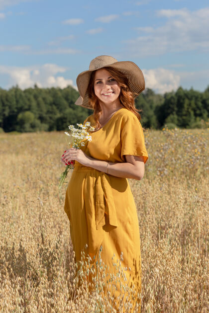 帽子在一个阳光明媚的夏日 一位年轻漂亮的孕妇穿着黄色的裙子 戴着黄色的帽子 走过一片麦田农村阳光生命