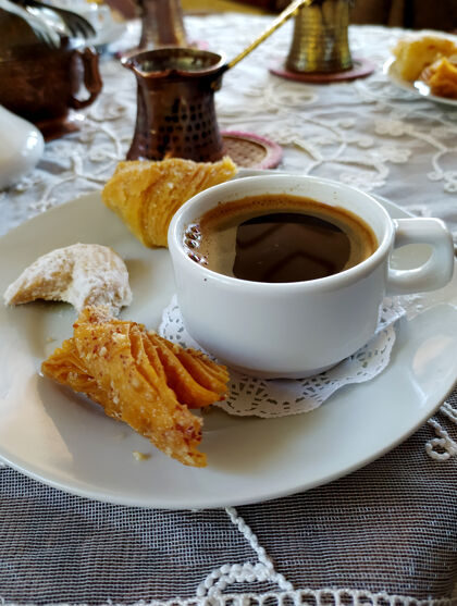 烹饪茶托上放着一杯咖啡和糖果 土耳其咖啡架上放着一块白色绣花桌布花边黄铜地