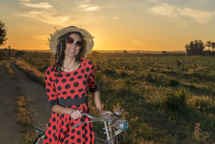 户外夕阳下 骑着自行车在乡间散步的女孩戴着墨镜微笑着女人草帽年轻