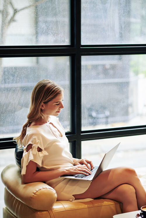 通信漂亮优雅的年轻女子坐在皮椅上 工作在笔记本电脑上 编程或回复电子邮件阅读在线企业家