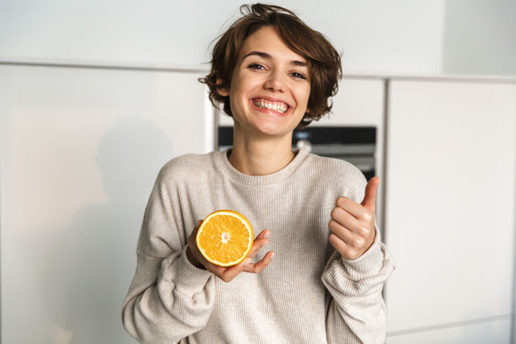 有机站在厨房里展示橙色水果的快乐女人维生素家庭主妇白种人