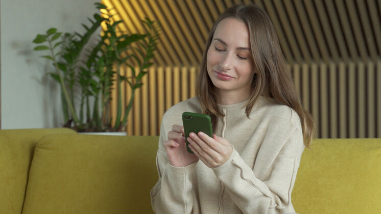 客厅女人坐在客厅的黄色沙发上用智能手机学习女孩聊天
