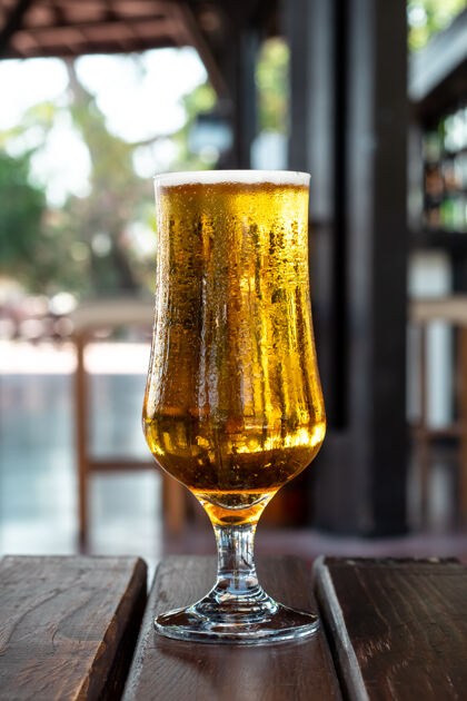 休闲酒吧里的木桌上放着一杯琥珀色的冰啤酒酒精饮料夏日休闲理念壶饮料满