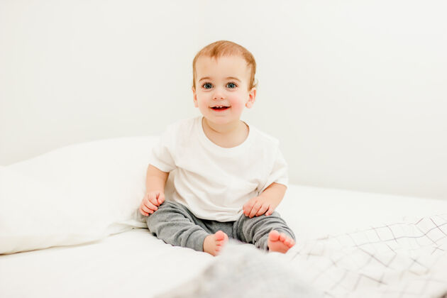 幼儿坐在家里床上的穿着白色T恤的婴儿室内可爱床