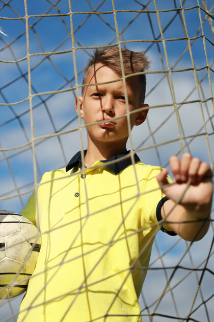 草地足球场上穿着黄色t恤的男孩足球运动员站在门口目标游戏足球