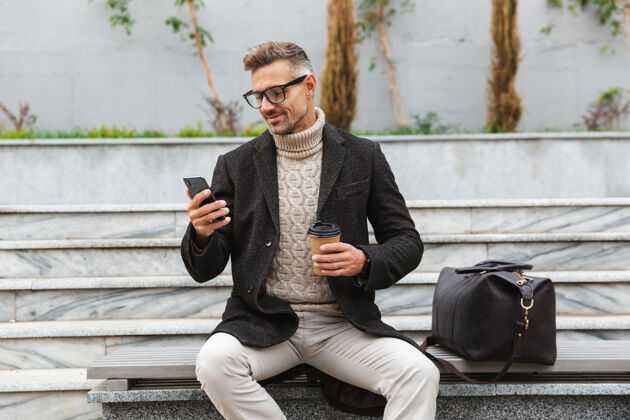 商人帅哥穿着夹克拿着手机 坐在户外喝外卖咖啡城镇夹克休闲