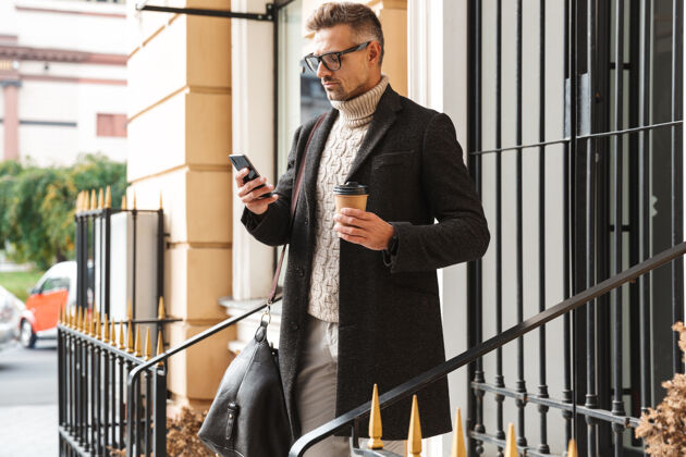 男士帅哥穿着外套走在户外 用手机 喝咖啡严肃成人吸引力