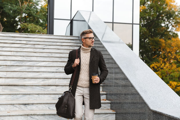 外卖30多岁的聪明人戴着眼镜 穿过城市街道 拿着外卖咖啡休闲城市夹克