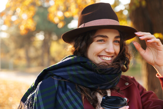 美丽美丽的年轻女子戴着帽子在秋天的公园散步 手里拿着一杯外卖咖啡茶季节帽子