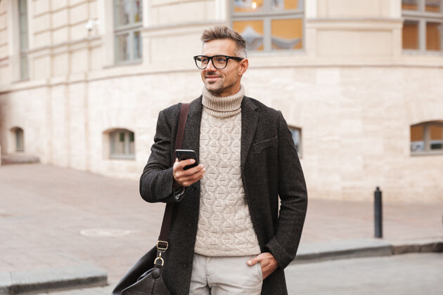 年轻帅哥穿着外套走在户外 手里拿着手机时尚步行短信