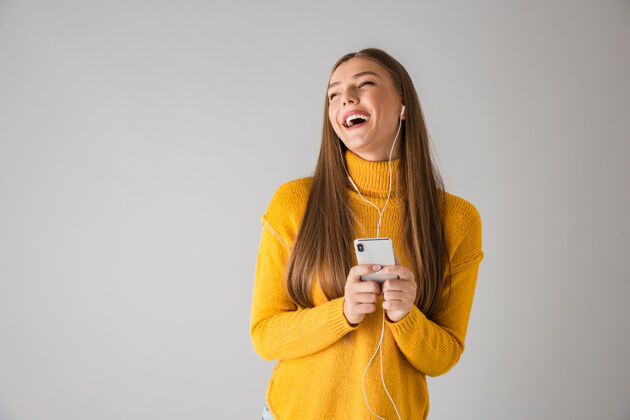 时尚一个美丽快乐的年轻女子用手机隔着灰色的墙被孤立的画面电话毛衣手机